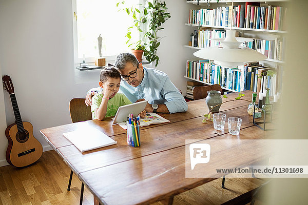 Vater und Sohn mit digitalem Tablett am Tisch