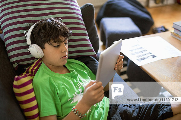 Junge  der Musik über ein digitales Tablett hört  während er sich zu Hause auf dem Sofa ausruht.