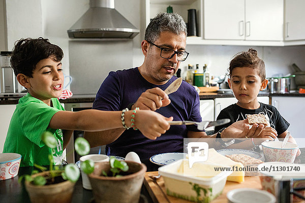 Vater und Söhne beim Auftragen von Butter auf Cracker am Esstisch