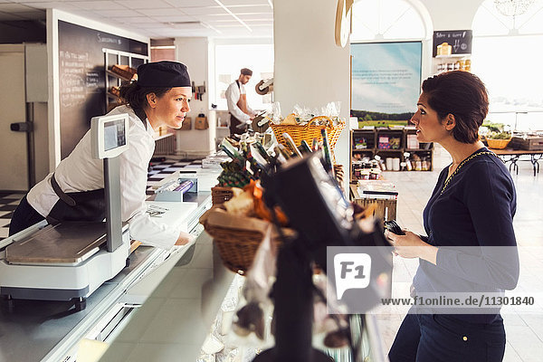 Side view of woman talking to saleswoman at counter at grocery store