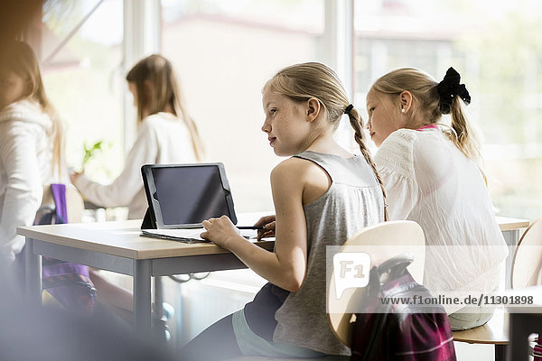 Rear view of girls sitting on desk against window in classroom