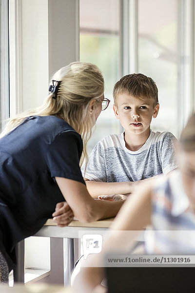 Lehrer assistierender Junge am Schreibtisch mit Mädchen im Vordergrund