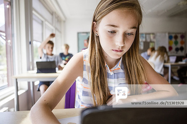 Schülerin mit digitalem Tablett am Schreibtisch im Klassenzimmer