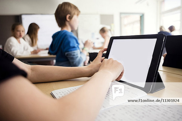 Cropped image of boy using digital tablet in classroom