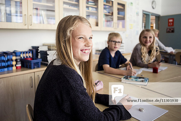 Happy girl sitting with friends at desk in classroom