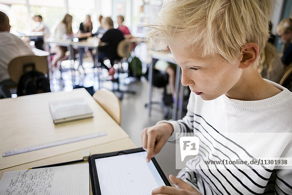 Junge mit digitalem Tablett am Schreibtisch im Klassenzimmer