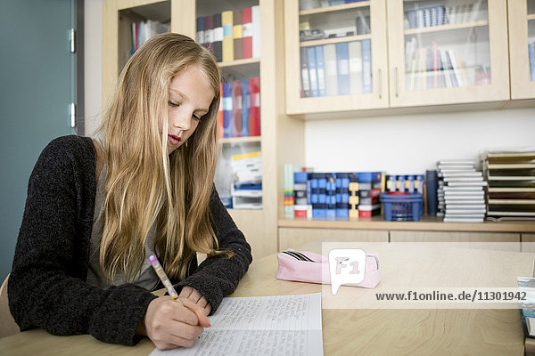 Mädchen schreiben im Buch auf dem Schreibtisch im Klassenzimmer