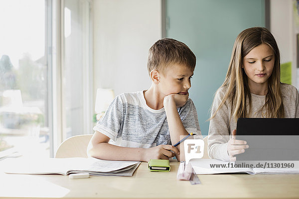 Junge schaut  während Mädchen mit Tablette am Schreibtisch im Klassenzimmer sitzt.