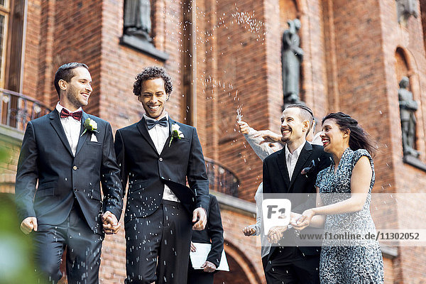 Low angle view of happy newlywed gay couple walking while friends throwing confetti