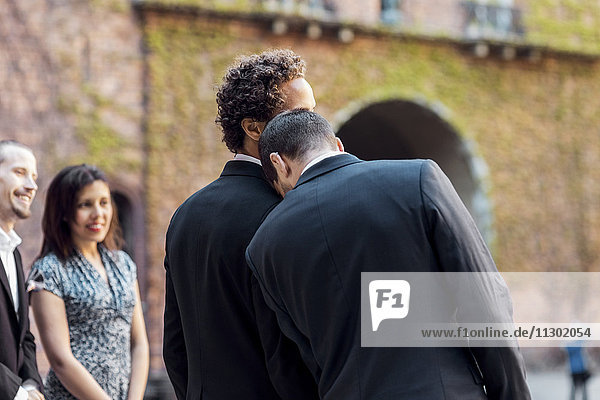 Rückansicht eines schwulen Mannes  der sich während der Hochzeit auf die Schulter des Partners stützt.
