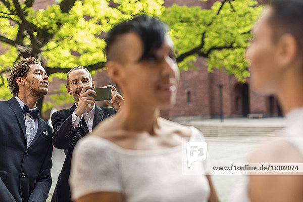 Männlicher Freund fotografiert lesbisches Paar während der Hochzeitszeremonie