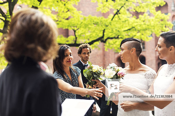 Lesbisches Ehepaar überreicht Blumensträuße an Gäste während der Hochzeitszeremonie