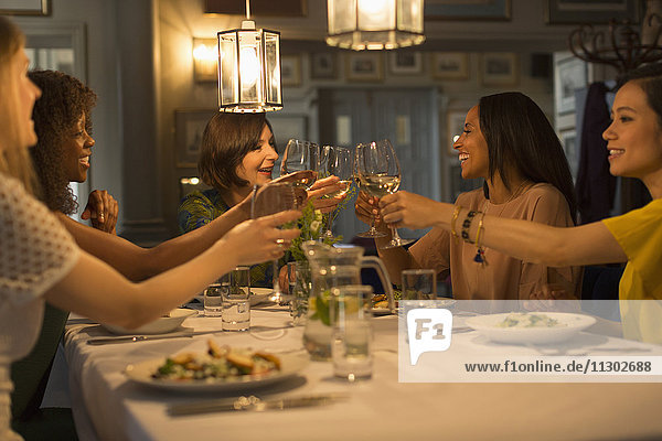 Women friends toasting white wine glasses at restaurant table