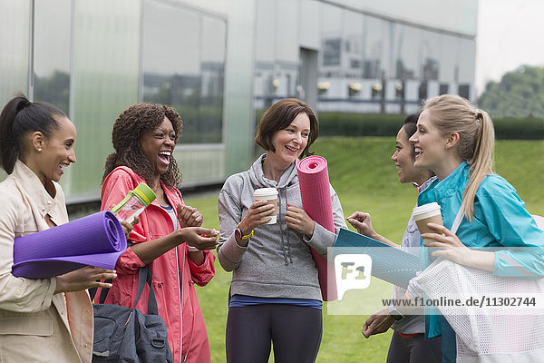 Women friends with yoga mats and coffee talking outside gym