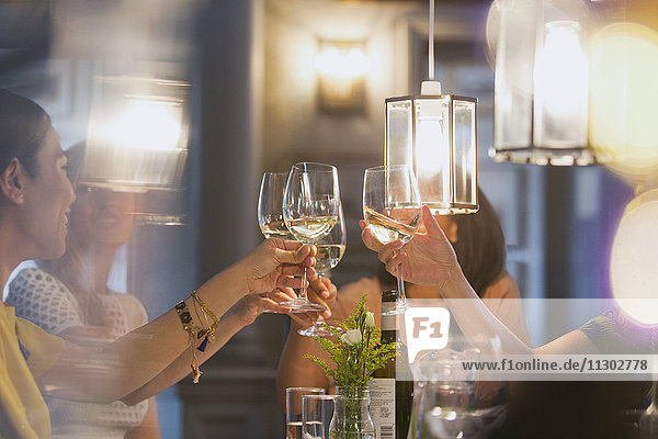 Weibliche Freunde stoßen auf Weißweingläser an  die am Restauranttisch speisen.