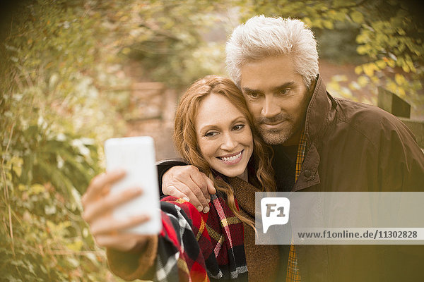 Paar  das sich umarmt und ein Selfie mit einem Fotohandy im Garten macht