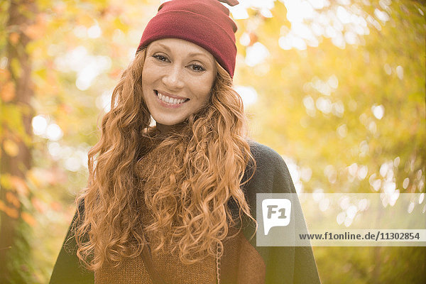 Porträt lächelnde Frau mit Strumpfmütze unter Herbstbäumen
