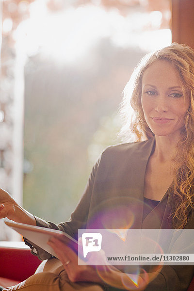 Porträt einer lächelnden Frau  die ein digitales Tablet in einem sonnigen Fenster benutzt