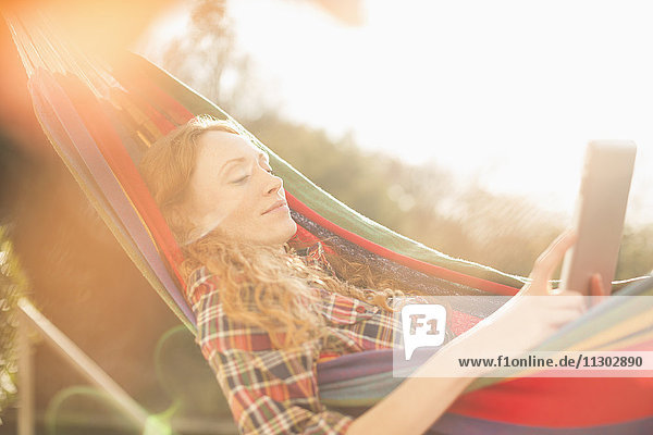 Frau entspannt sich in sonniger Hängematte mit digitalem Tablet
