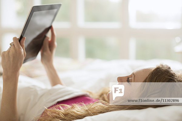 Frau liegt im Bett und benutzt ein digitales Tablet