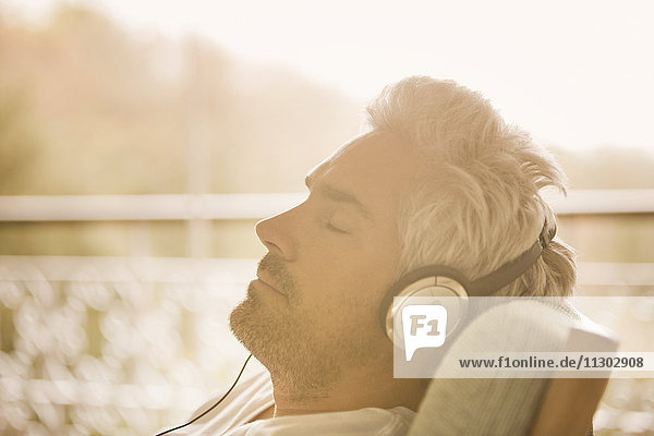 Gelassener Mann mit Kopfhörern beim Musikhören auf einer sonnigen Veranda