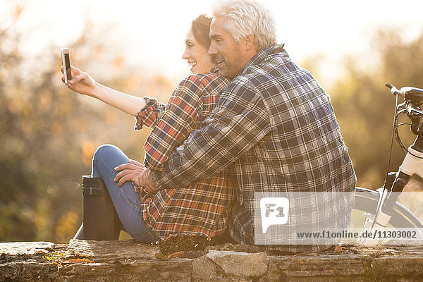 Zärtliches Paar umarmt Aufnahme selfie mit Kamera-Handy im Herbst Park