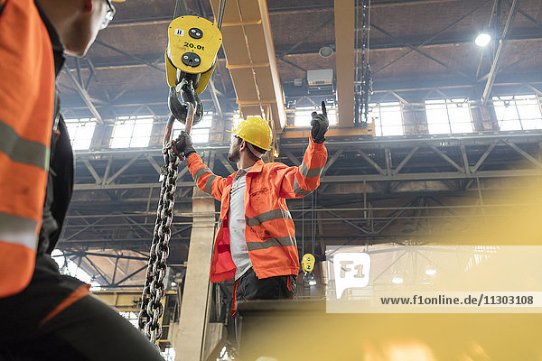Steel workers fastening chain to crane in factory