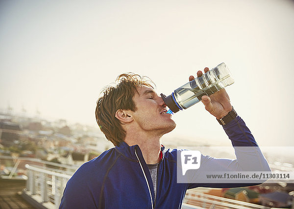 Männlicher Läufer trinkt Wasser auf einer städtischen Fußgängerbrücke