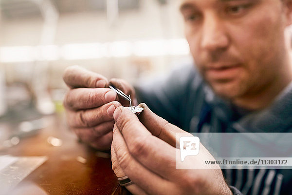 Fokussierter männlicher Juwelier  der Schmuck in der Werkstatt zusammenbaut.