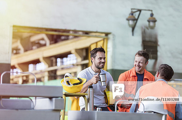 Lächelnde Stahlarbeiter genießen Kaffeepause in der Fabrik