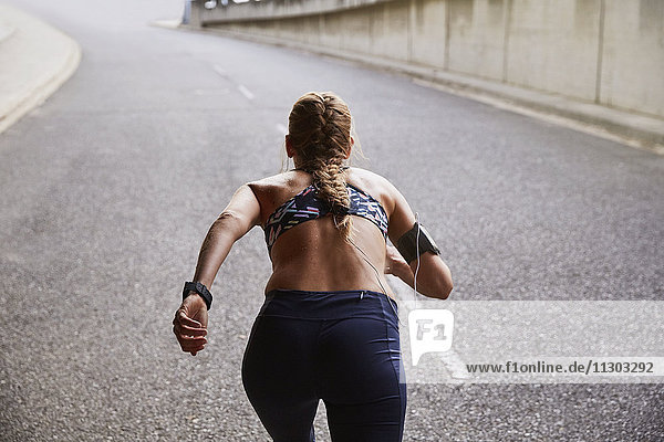 Fitte Läuferin mit mp3-Player-Armband beim Laufen auf einer städtischen Straße