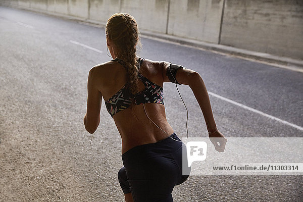 Fitte Läuferin in Sport-BH und mp3-Player-Armband beim Laufen auf einer städtischen Straße