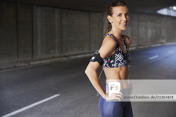 Porträt lächelnd fit weibliche Läuferin in Sport-BH mit mp3-Player-Armband und Kopfhörer in städtischen Tunnel