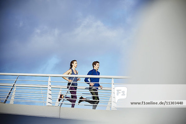 Runner couple running on sunny footbridge