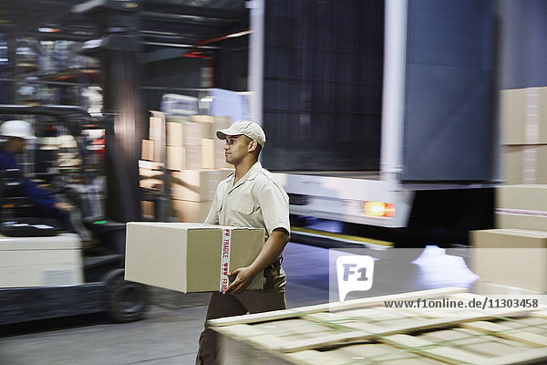 Arbeiter trägt Karton an der Laderampe eines Vertriebslagers
