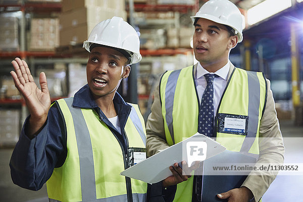 Manager and worker with clipboard talking in distribution warehouse