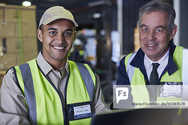 Porträt eines lächelnden Managers und eines Arbeiters  der einen Laptop in einem Vertriebslager benutzt