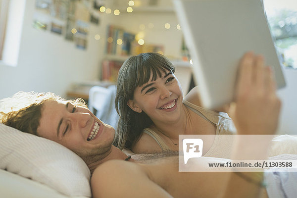 Lächelndes junges Paar benutzt digitales Tablet im Bett