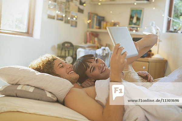 Lächelndes junges Paar  das im Bett liegt und ein digitales Tablet benutzt