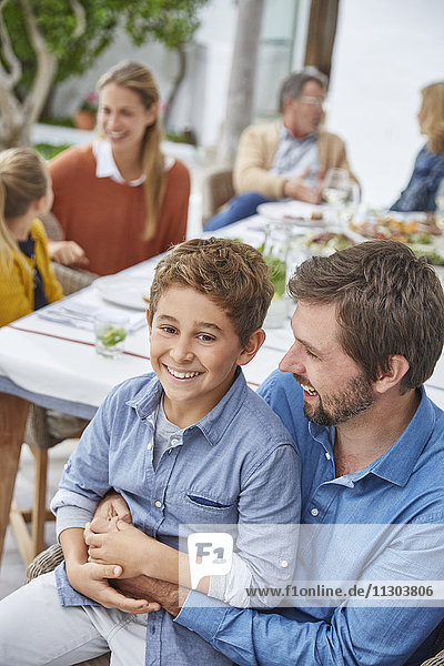 Portrait lächelnder Vater und Sohn beim Mittagessen im Innenhof