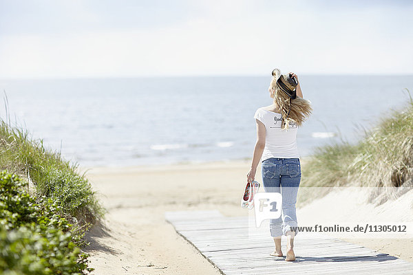 Junge Frau geht am Strand mit Meer im Hintergrund