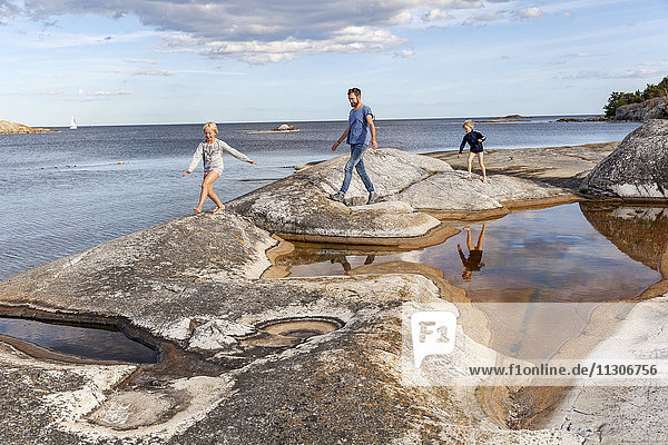 Vater und zwei Söhne spazieren auf Felsen an der Küste