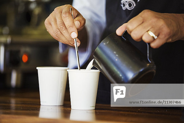 Close up of hot milk being poured from a jug into a paper cup.