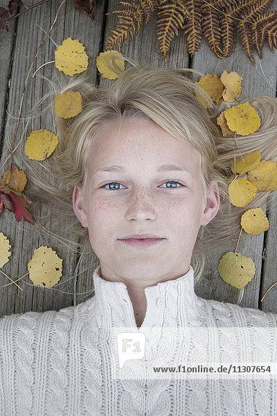 Porträt eines blonden Mädchens  das auf einem Holzsteg liegt  umgeben von Herbstblättern