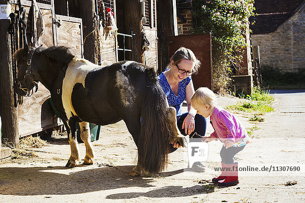 Woman showing a toddler a pony's shoe.