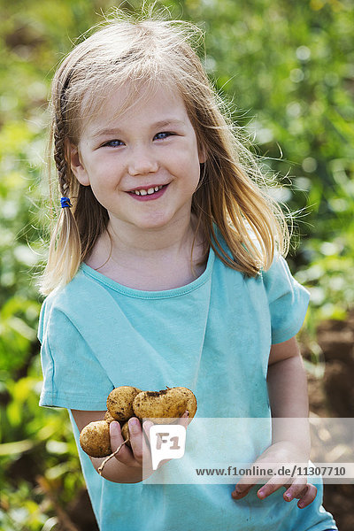 Ein Mädchen hält Kartoffeln in einem Gemüsebeet.