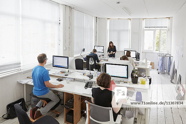 Ein modernes Büro  Arbeitsplätze für das Personal. Erhöhte Ansicht von sechs Personen  die an Schreibtischen sitzen. Ein Mann  der einen ergonomischen Kniestuhl benutzt.