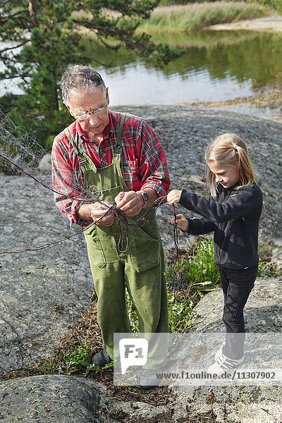 Girl helping grandfather repairs fishing net