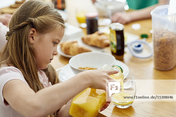 Eine Familie beim Frühstück. Ein Mädchen gießt Orangensaft in ein Glas.