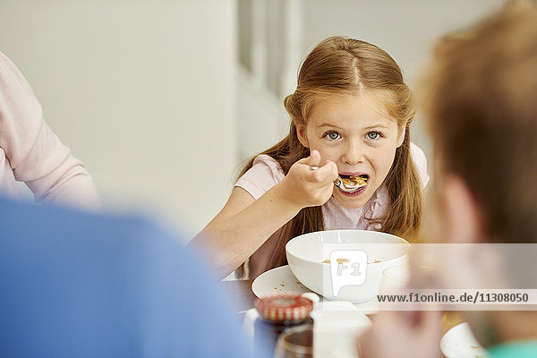 A family eating breakfast. A girl eating cereal with a spoon.